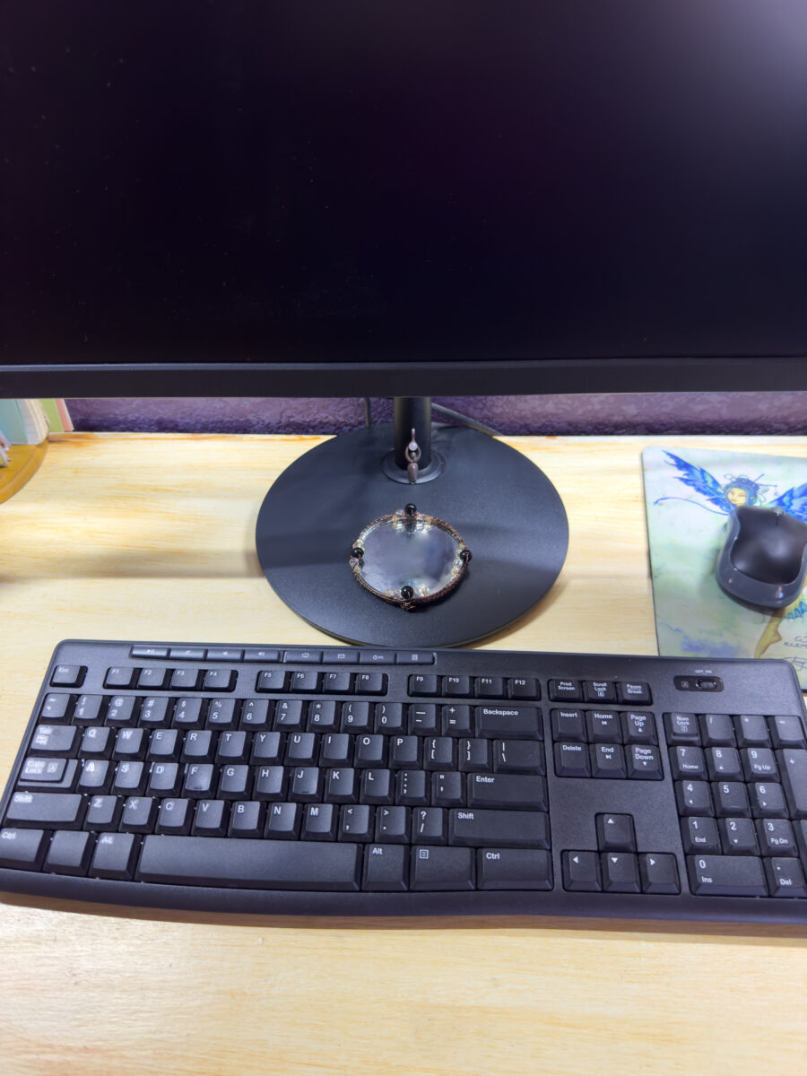 Handmade wire-wrapped mirror with tourmaline, clear quartz, and citrine, charged for protection, beneath a computer monitor