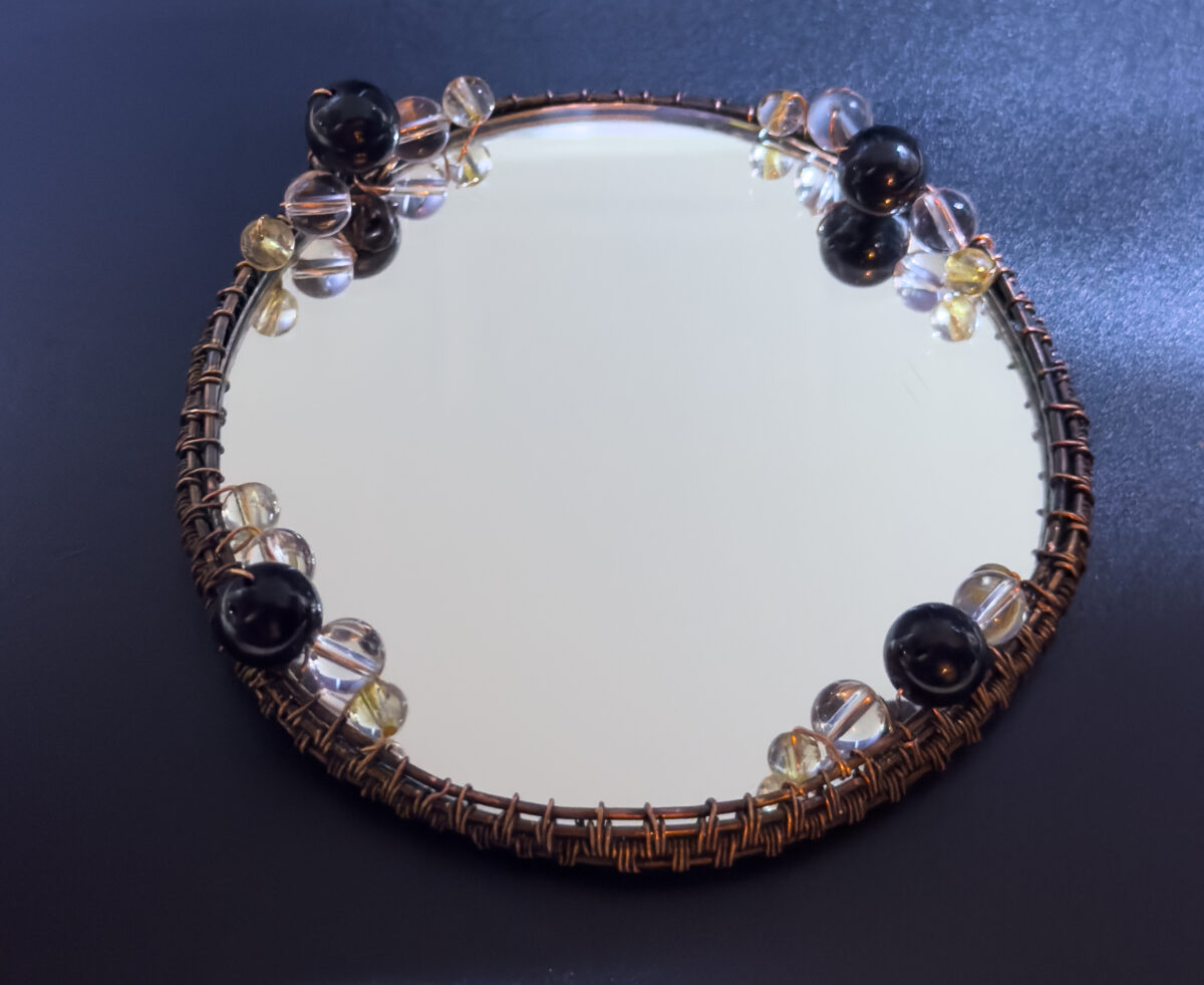 Close-up of handmade copper wire-wrapped mirror with tourmaline, clear quartz, and citrine